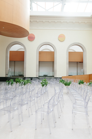 AGO Toronto Wedding Photography. The Art Gallery of Ontario makes a stunning and elegant backdrop for a couple's vows. Shown in this image are the Louis ghost guest chairs and green foliage in tall silver vases lining the aisle.