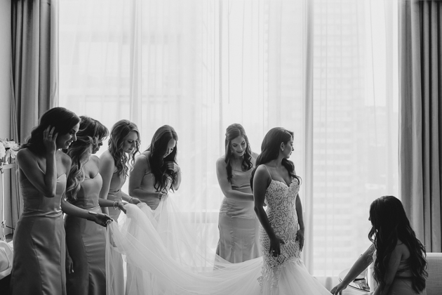 Bridesmaids helping the bride to put on her wedding dress at Four Seasons Hotel Toronto